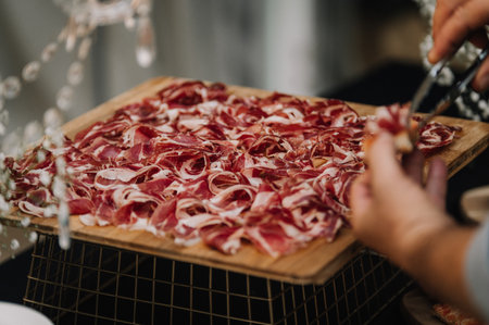 A closeup of a person taking a piece of the sliced delicious Iberian ham on the wooden boardの写真素材