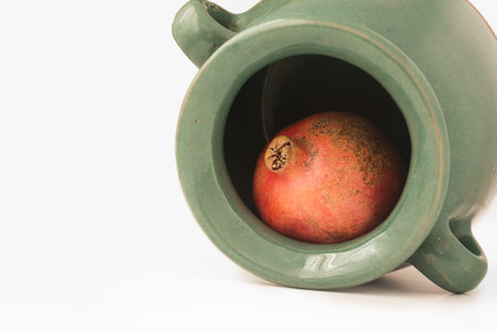 A pomegranate inside the greenish earthen jar isolated on white background