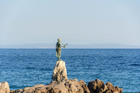 Rocky coastline with statue of a woman with seagull in Opatija, Croatia.の写真素材