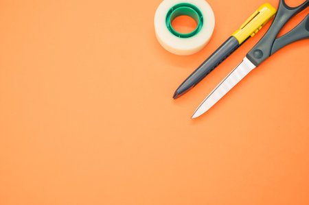A closeup shot of scissors adhesive tape and a utility knife on an orange backgroundの写真素材