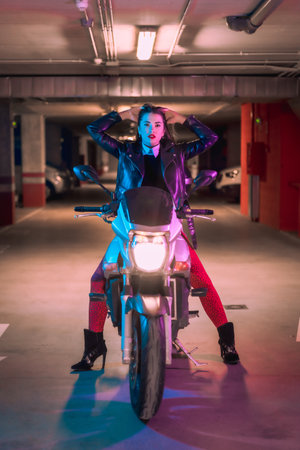 A Spanish woman in a leather jacket posing on a motorcycle with neon lightsの写真素材