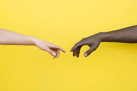 A shot of a white-skinned hand and a black-skinned hand about to touch on a yellow backgroundの写真素材