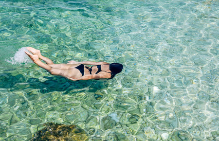 Young tourist swimming and diving near beautiful hidden beach with transparent water.の写真素材
