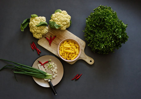 A top view of raw pasta in a bowl, chili pepper and cauliflower on a board, boxwood, and scallionsの写真素材