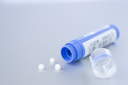 A blue homeopathic medicine container opened on a white surface with three pills on it. Blank space to the leftの写真素材