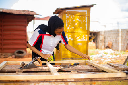 A female African professional carpenter smiling as she takes a measurement of woodの写真素材