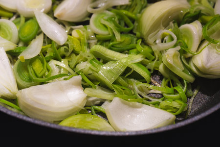 A closeup shot of quartered onions and green leek in a panの写真素材