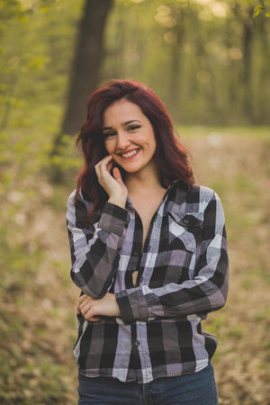 A vertical shot of a young caucasian female with an unbuttoned shirt posing in the forestの写真素材