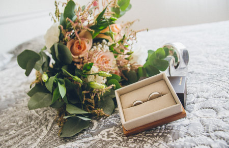 A selective focus shot of silver wedding rings and a bridal bouquet on a bed