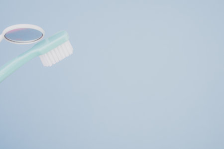A blue toothbrush next to a dental mouth mirror on pastel blue surface for a copy spaceの写真素材