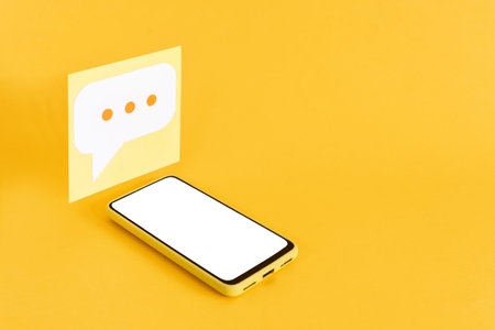 The paper speech bubbles and a smartphone with a blank screen on a yellow background.の写真素材