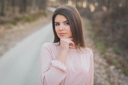 A shallow focus shot of a caucasian woman wearing a beautiful pink dress, posing on a country road in Bosnia and Herzegovinaの写真素材