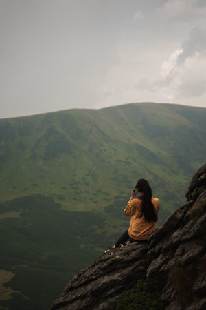 A back view of an adventurous hiker female sitting on the rocky cliff enjoying the beautiful viewの写真素材