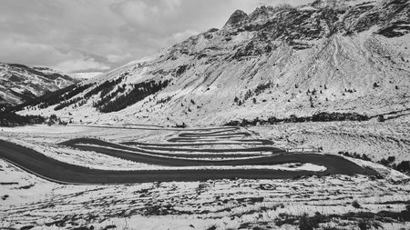 A grayscale shot of a landscape with a curvy road and a mountain in winterの写真素材