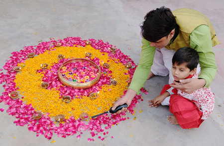 The Indian male with his son creating rangoli using candles, marigold and pink rose petalsの写真素材