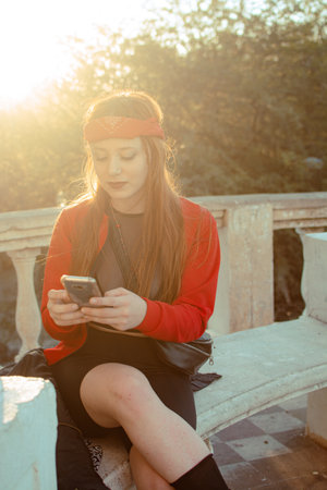 A young woman with red lipstick and a hair band looking at her phoneの写真素材