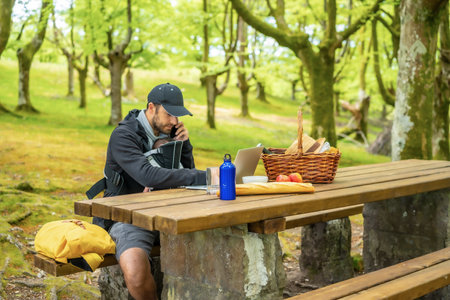A young caucasian father talking with his phone and teleworking in a parkの写真素材