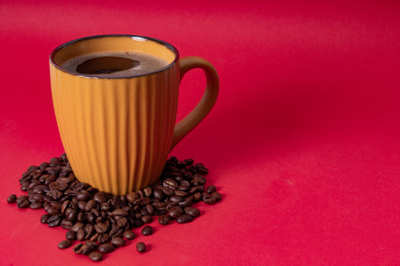 A closeup shot of a cup of hot coffee and coffee beans isolated on a red background