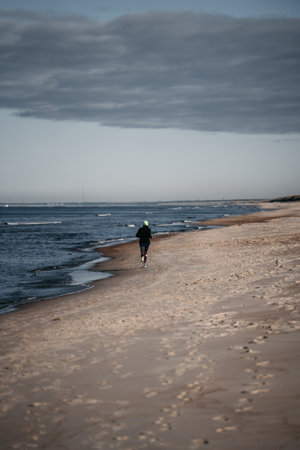 A rear view of man running on the seashore under a gloomy skyの写真素材