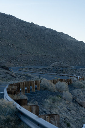 A vertical shot of a swirly road under a hill with dry bushes