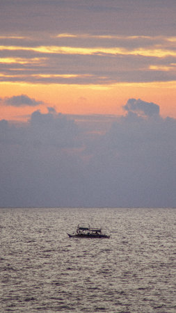 A vertical shot of a calm sea with a floating boat on a pink sunset backgroundの写真素材