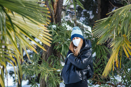 A shallow focus shot of a young female in a white face mask surrounded by palm treesの写真素材