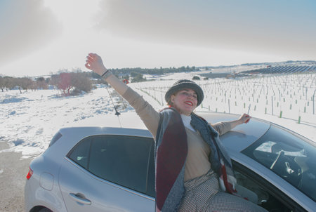 A cheerful lady wearing winter clothing leaning out of the car window and enjoying the road tripの写真素材