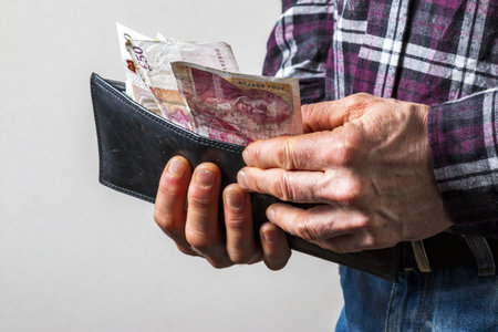man checking wallet for cash on a white background wearing blue jeans and check shirt casually...