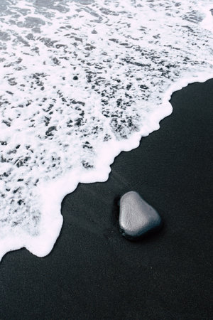 A vertical shot of foamy waves washing the black sand beach