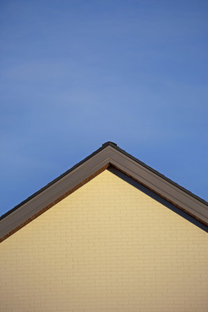 A vertical shot of the building roof in a triangle form with light yellow external walls in blue sky...