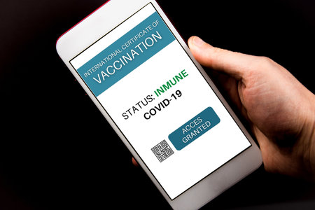 Hands of a man holding smartphone with the certificate of vaccination against Covid-19. Traveling in a pandemicの写真素材