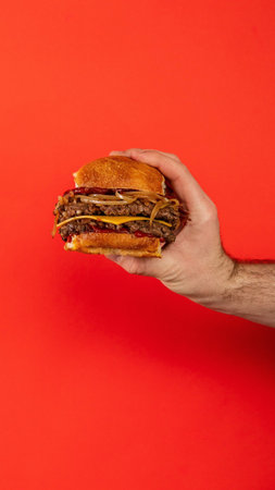 A vertical shot of a male hand holding a hamburger on an isolated red backgroundの写真素材