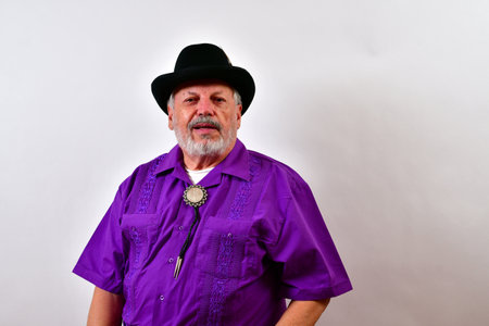 An elderly successful gentleman is posing in a purple shirt and black hatの写真素材