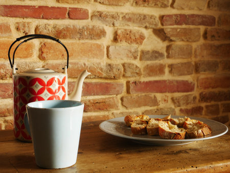 A closeup of a teapot with a cup and a plate of sliced bread on the wooden drawerの写真素材