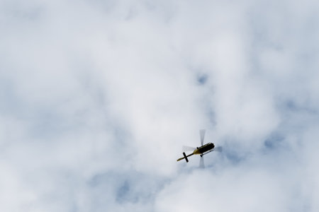 A low angle shot of a helicopter flying under a cloudy bright skyの写真素材