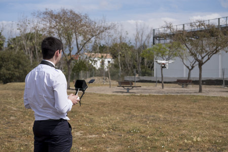A young male in a flight school uniform piloting during a drone flight practice in a field with...