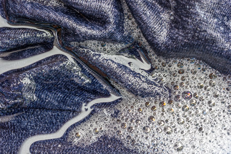 A closeup of wet clothes with foam and bubbles in the washing machine