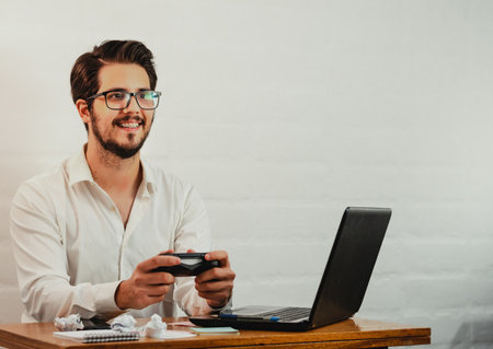 A young Caucasian male in glasses playing video game console while working in at home