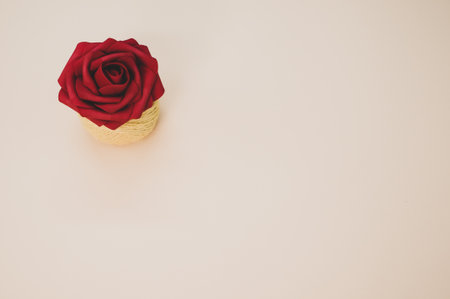 A closeup of an artificial red rose on a thread spool and pastel peach surface for a copy spaceの写真素材