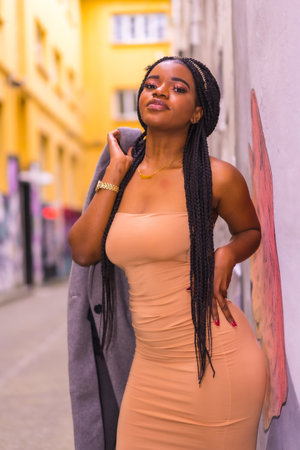 A vertical shot of an African-American female in an elegant posing in the street with her jacketの写真素材