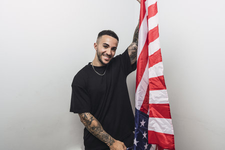 A young proud Hispanic man holding a US flag against a white backgroundの写真素材