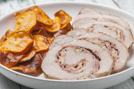 A closeup of stuffed pork tenderloin with bacon, nuts, and crisp potatoes on a plaの写真素材