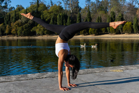 brunette woman in exercise clothes practicing yoga in the morning and in the background a lake with ducks. Handstand stretching legs. concept of balance and elasticity.の写真素材