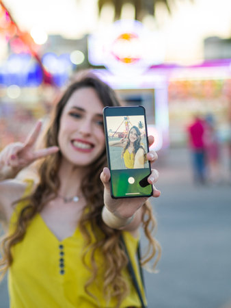 A Beautiful caucasian girl posing with her phone taking a selfie at the amusement parkの写真素材