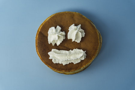 A closeup of pancakes with a smiley face drawn with whipped cream, on a blue surfaceの写真素材
