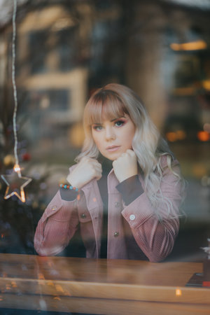 A vertical shot of a young blonde caucasian female posing in a pink coat