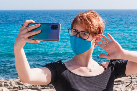 A young caucasian female in a face mask taking a selfie at the beachの写真素材