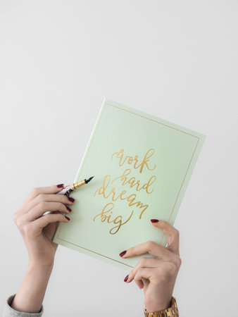 A vertical shot of female hands holding a green notebook with an inspirational quote and pen isolated on a white backgroundの写真素材
