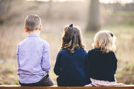A back view of a little boy and two girls sitting on a benchの写真素材