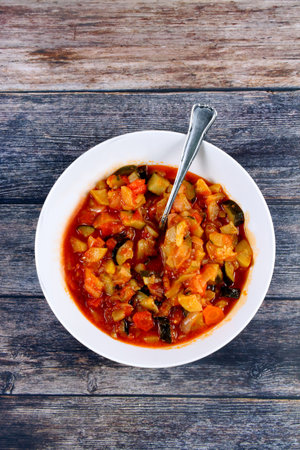 A top view of a bowl of vegetable stew with a spoon on a wooden surfaceの写真素材